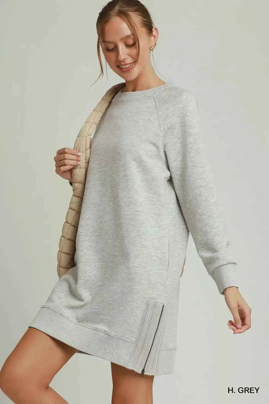 Woman wearing a heather grey sweatshirt dress with side crochet trim, zipper details, pockets, and long sleeves by Umgee. Side View