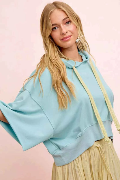 Woman wearing a light blue washed terry short sleeve hoodie top with drawstring hood and relaxed oversized fit by BiBi. Side View