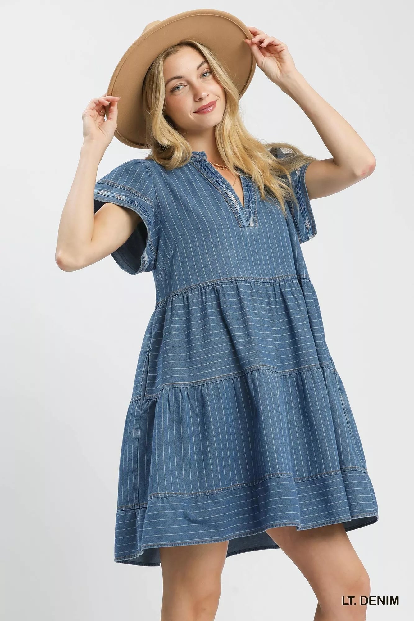 Woman wearing a light denim pinstripe chambray tiered babydoll dress with flutter sleeves and pockets by Umgee