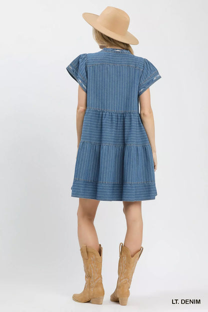 Woman wearing a light denim pinstripe chambray tiered babydoll dress with flutter sleeves and pockets by Umgee Back View