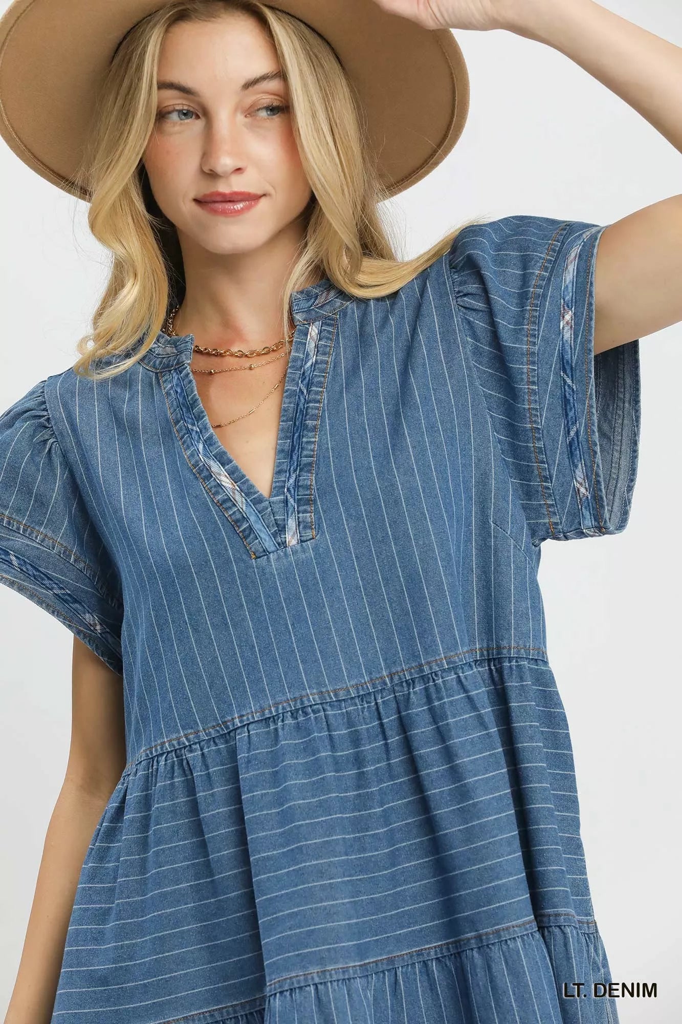 Woman wearing a light denim pinstripe chambray tiered babydoll dress with flutter sleeves and pockets by Umgee Close View