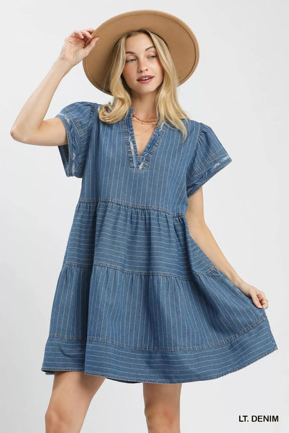 Woman wearing a light denim pinstripe chambray tiered babydoll dress with flutter sleeves and pockets by Umgee Front View