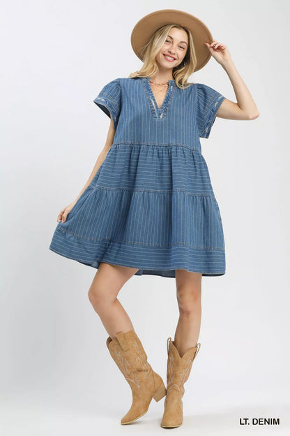 Woman wearing a light denim pinstripe chambray tiered babydoll dress with flutter sleeves and pockets by Umgee Full View