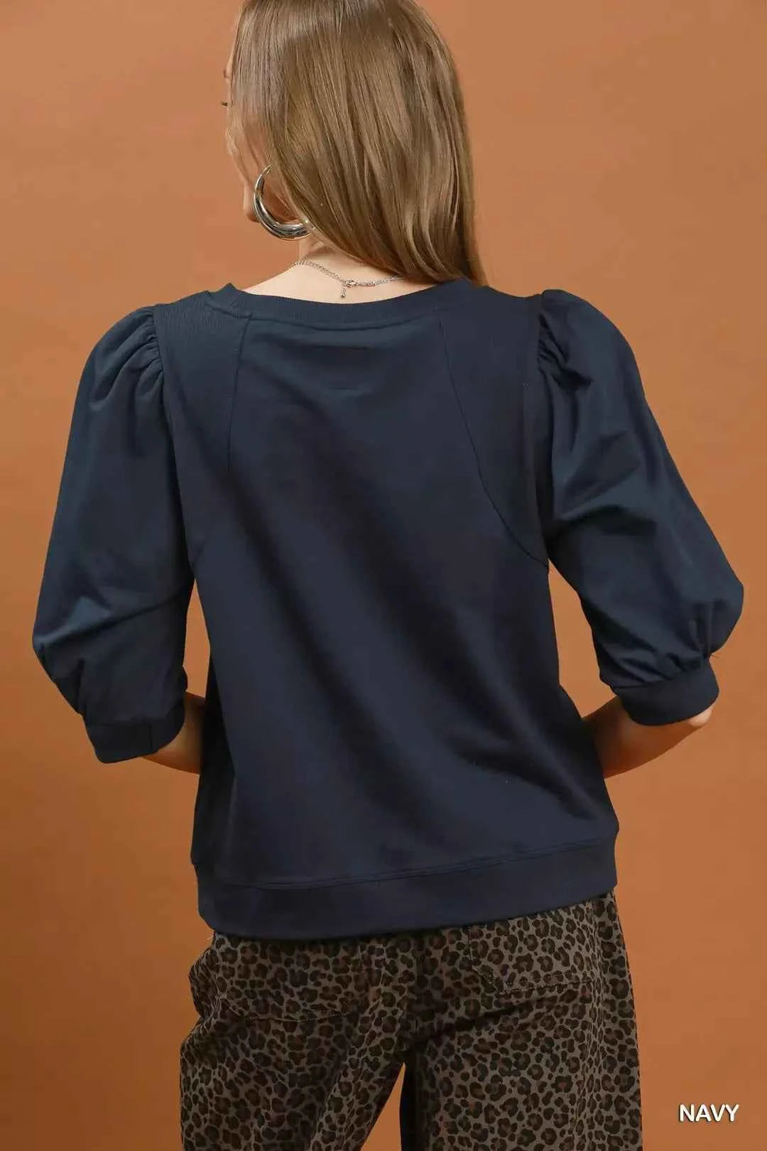 Woman wearing a navy puff sleeve cotton sweatshirt by Umgee paired with leopard print pants for an elevated casual outfit. Back View