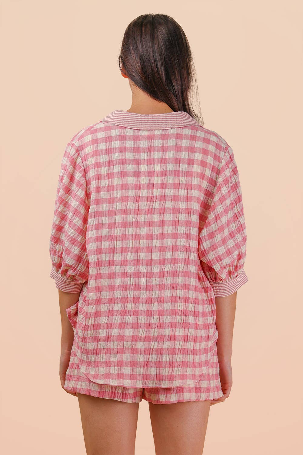 Woman wearing a pink and white gingham button-down shirt and matching drawstring shorts set back view