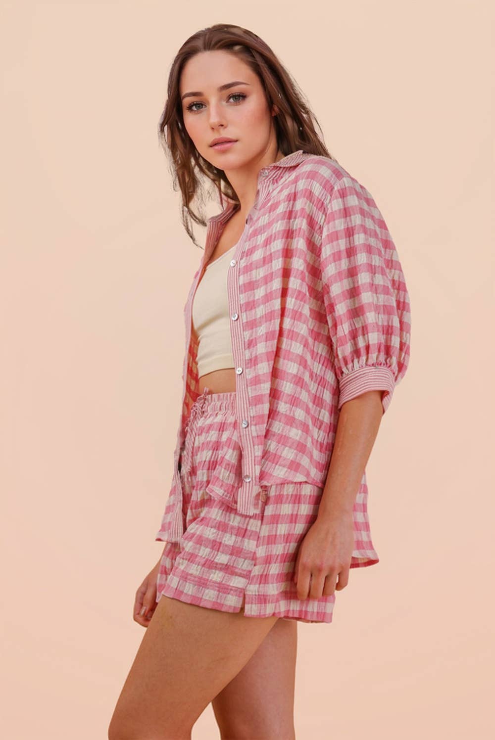 Woman wearing a pink and white gingham button-down shirt and matching drawstring shorts set side view