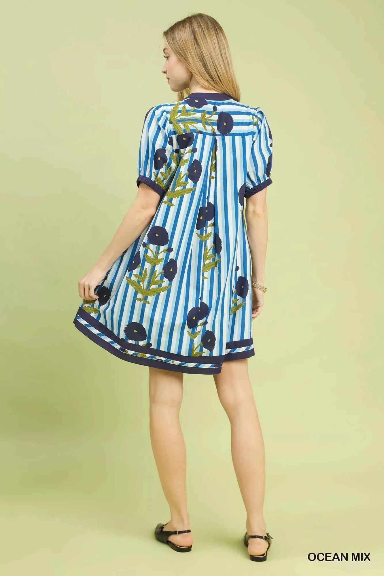 Woman wearing an Ocean Blue mixed floral and stripe print cotton dress with a split V-neckline and contrast trim by Umgee. back view