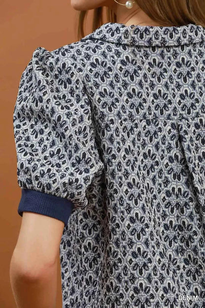 Woman wearing an Umgee denim blue printed puff sleeve collared blouse with a floral-inspired print and V-neck collar. close View
