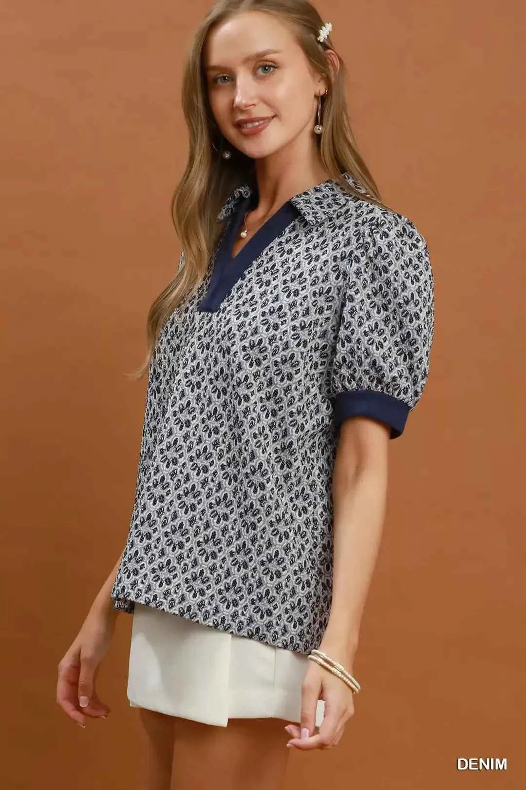 Woman wearing an Umgee denim blue printed puff sleeve collared blouse with a floral-inspired print and V-neck collar. Side View