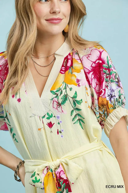 Woman wearing an Umgee ecru floral border print midi dress with a waist tie, puff sleeves, and colorful floral details. Close View