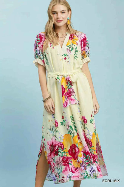 Woman wearing an Umgee ecru floral border print midi dress with a waist tie, puff sleeves, and colorful floral details. Front View