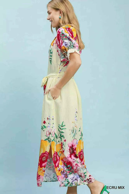 Woman wearing an Umgee ecru floral border print midi dress with a waist tie, puff sleeves, and colorful floral details. Side View