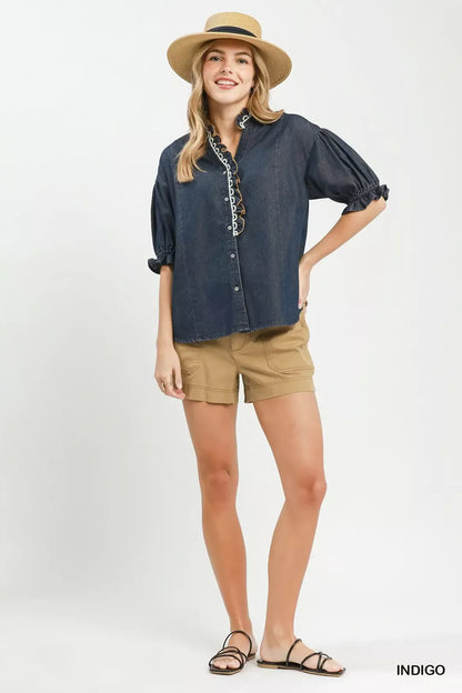 Woman wearing an Umgee indigo chambray button front blouse with lace trim neckline and puff sleeves styled with casual shorts. Full View