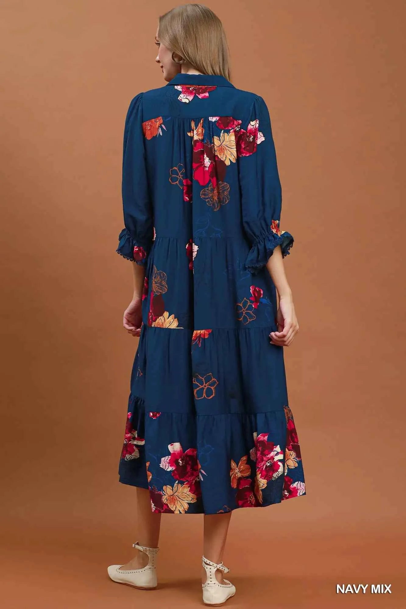 Woman wearing an Umgee navy floral tiered midi dress with puff sleeves, pockets, and a flowy feminine silhouette. Back View