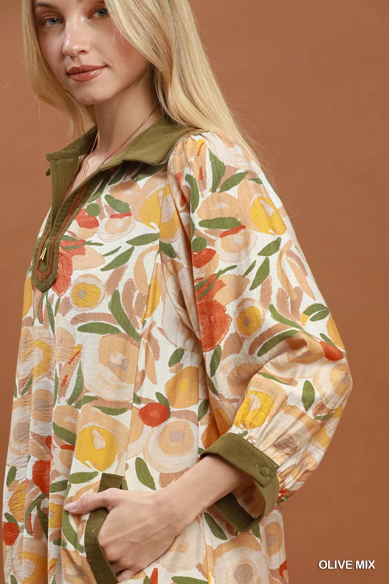 Woman wearing an olive floral contrast trim shift mini dress by Umgee featuring a relaxed silhouette, side pockets, three-quarter sleeves, and watercolor floral print. close view