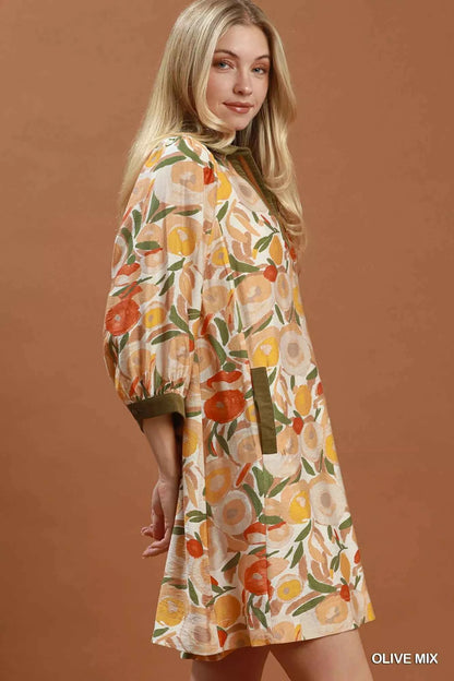 Woman wearing an olive floral contrast trim shift mini dress by Umgee featuring a relaxed silhouette, side pockets, three-quarter sleeves, and watercolor floral print. side view