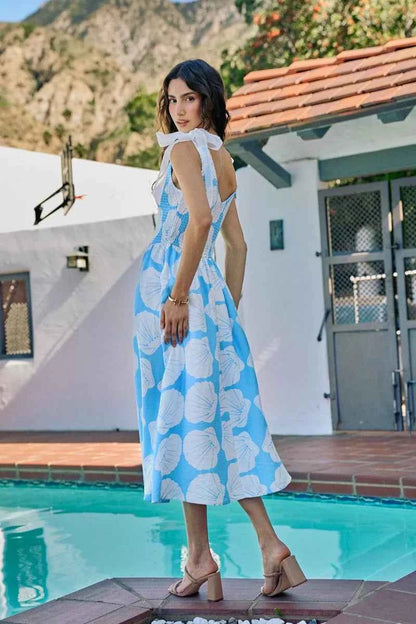 Woman wearing blue and white shell print midi dress by SO ME featuring a smocked bodice, tie shoulder straps, and flowy A-line silhouette. Back View