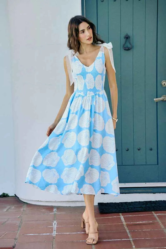 Woman wearing blue and white shell print midi dress by SO ME featuring a smocked bodice, tie shoulder straps, and flowy A-line silhouette. Front view