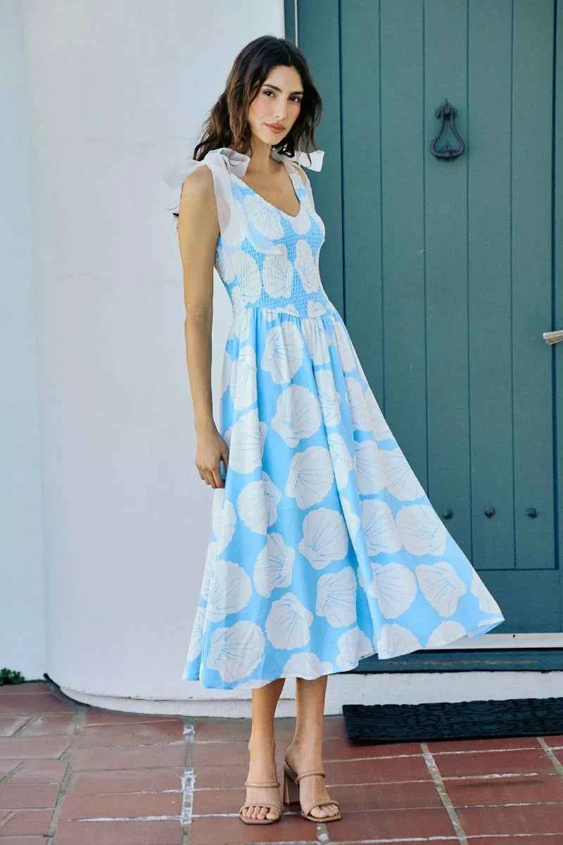Woman wearing blue and white shell print midi dress by SO ME featuring a smocked bodice, tie shoulder straps, and flowy A-line silhouette. Front View 2