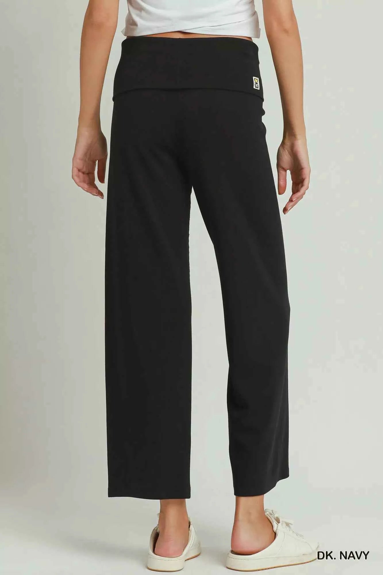 Woman wearing dark navy straight-leg pants with a folded waistband styled with white sneakers by Umgee. Back View