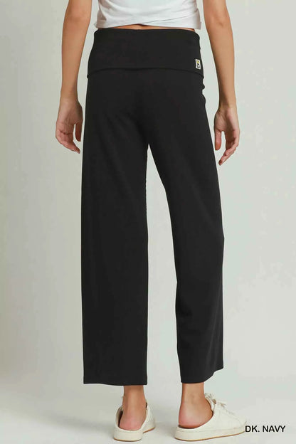 Woman wearing dark navy straight-leg pants with a folded waistband styled with white sneakers by Umgee. Back View