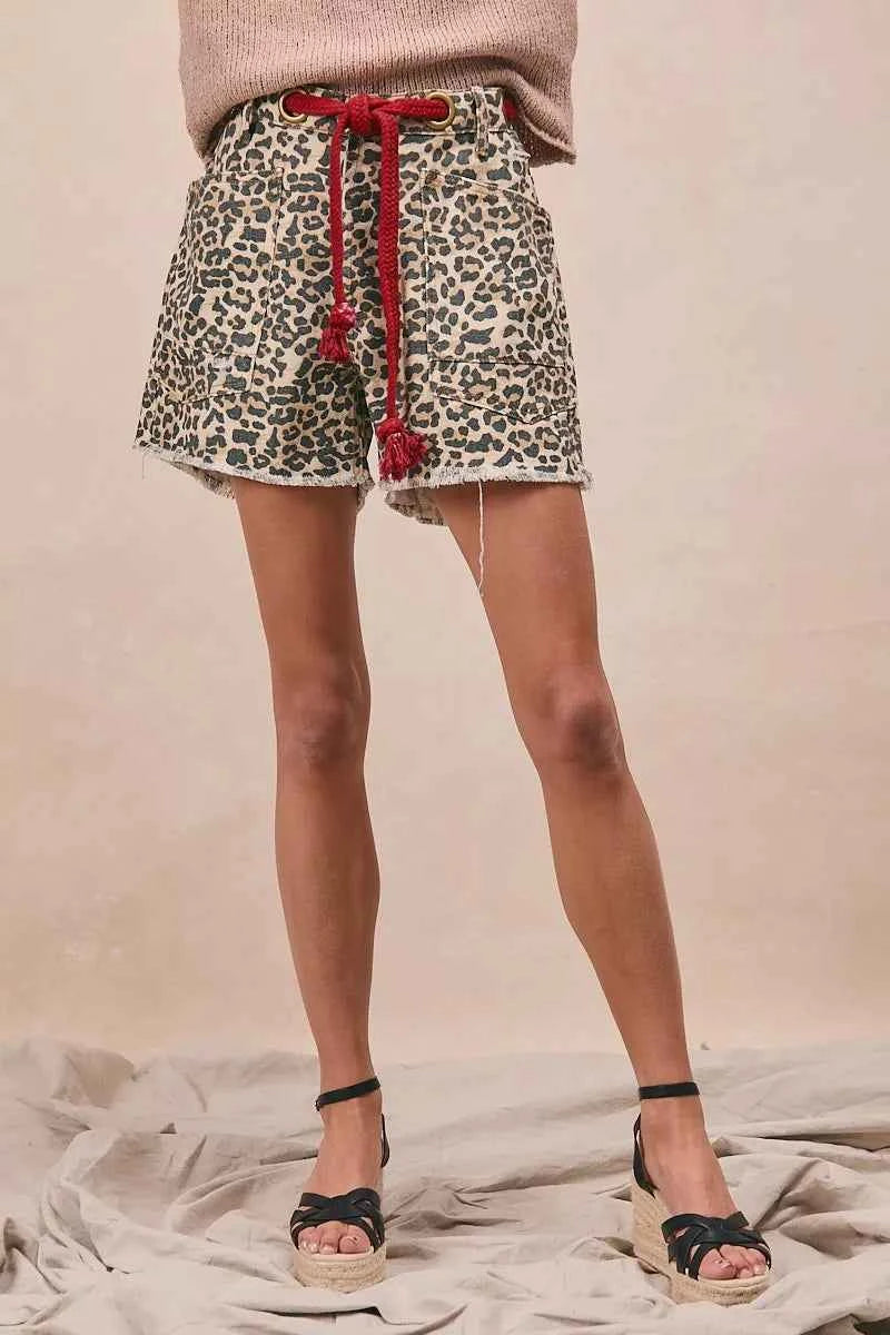 Woman wearing leopard print cotton shorts with a braided tassel waist belt, raw hem, and oversized front patch pockets by BiBi. Front view