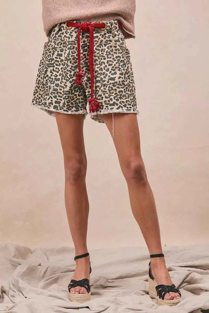Woman wearing leopard print cotton shorts with a braided tassel waist belt, raw hem, and oversized front patch pockets by BiBi. Front view