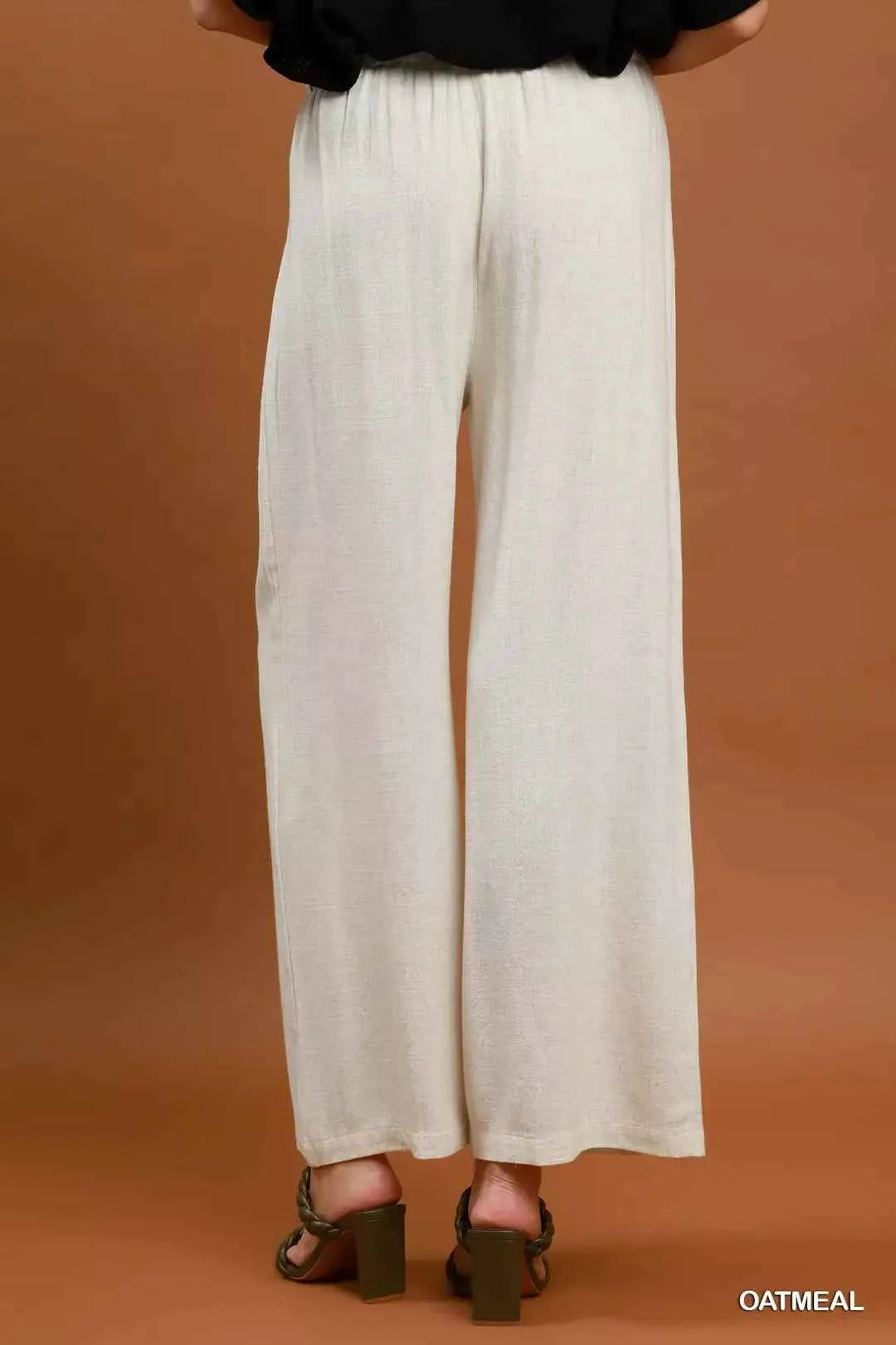 Woman wearing oatmeal high-waisted linen blend wide leg trousers with pleated front and pockets by Umgee. Back View