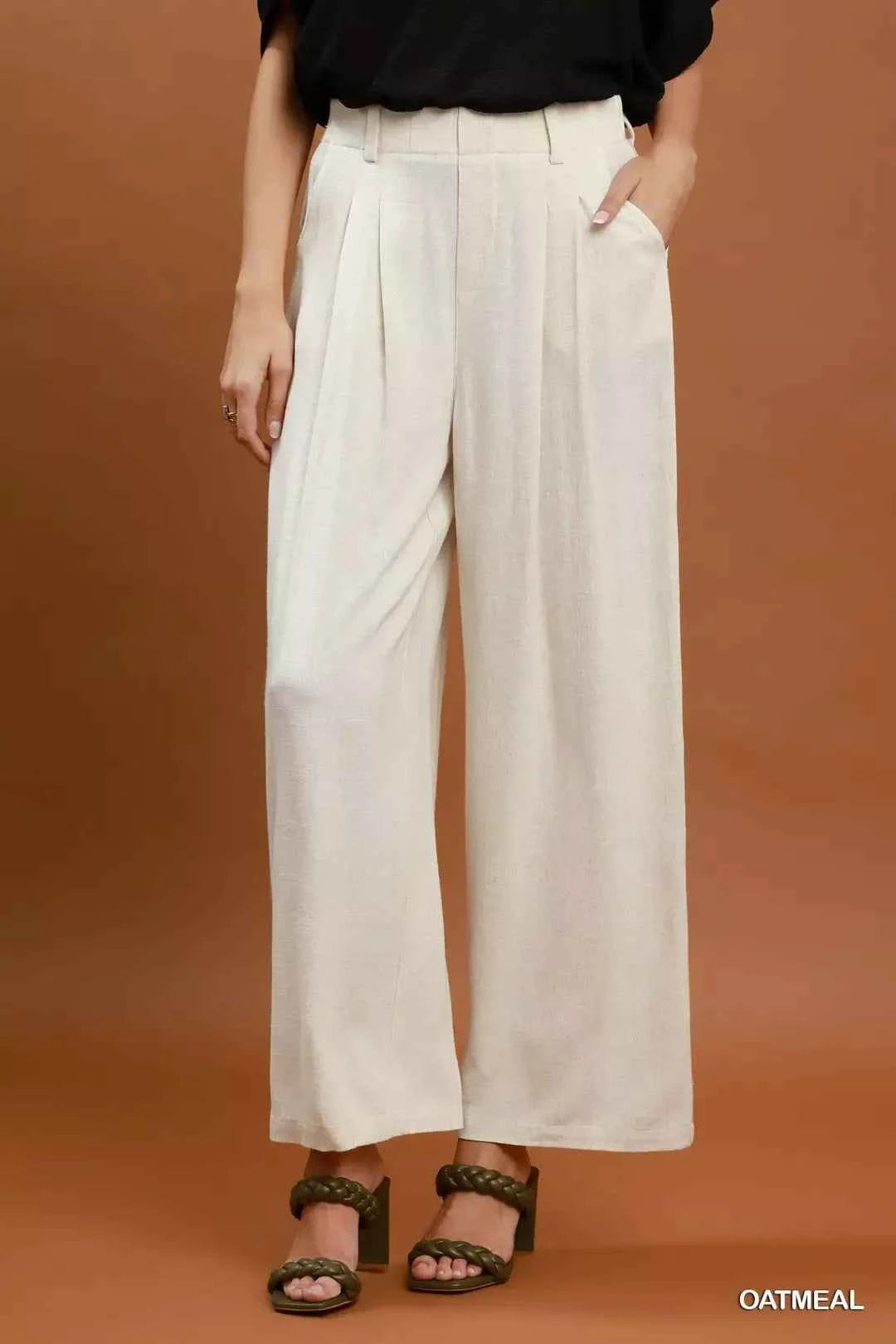 Woman wearing oatmeal high-waisted linen blend wide leg trousers with pleated front and pockets by Umgee. Front View