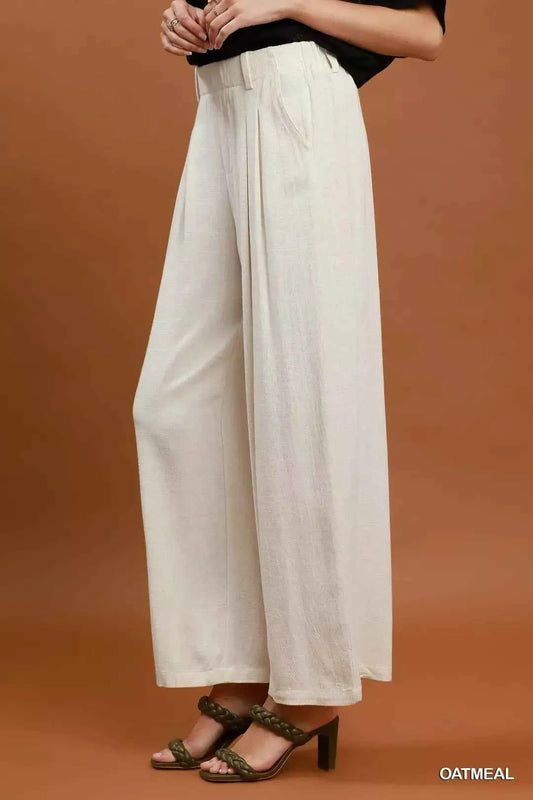 Woman wearing oatmeal high-waisted linen blend wide leg trousers with pleated front and pockets by Umgee. Side View
