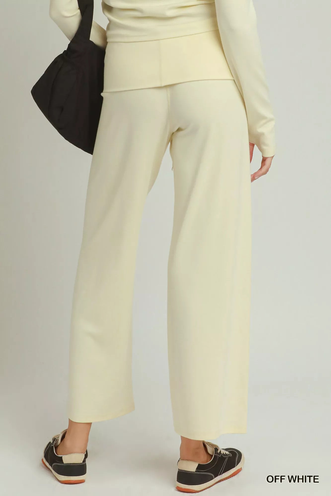 Woman wearing off white straight-leg pants by Umgee styled with black sneakers and a coordinating knit top. Back View