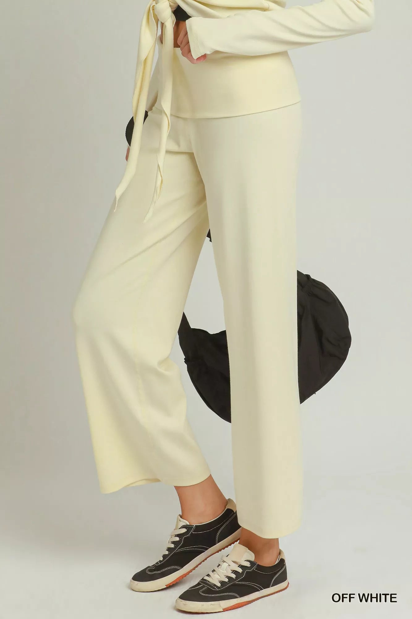 Woman wearing off white straight-leg pants by Umgee styled with black sneakers and a coordinating knit top. Side View