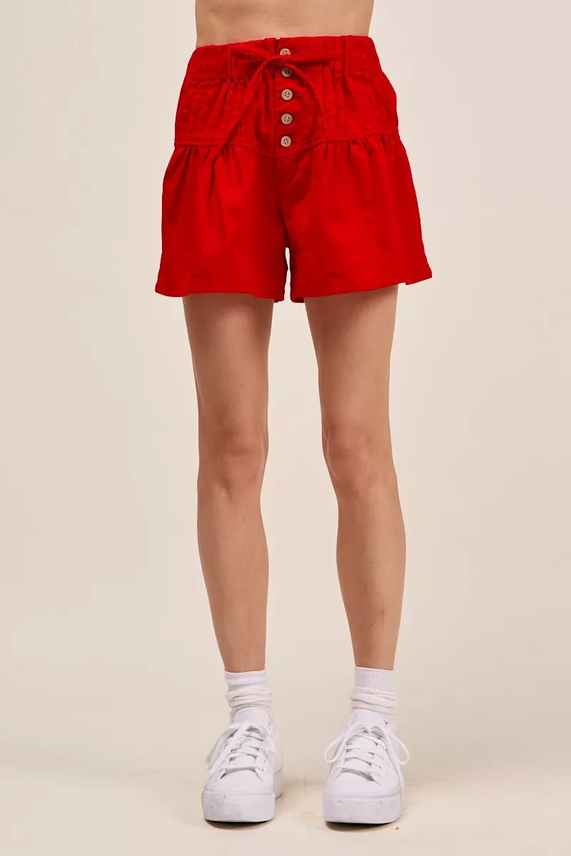 Woman wearing red high waist shorts with pintuck detailing, button-front accents, elastic waistband, and adjustable waist tie. full View