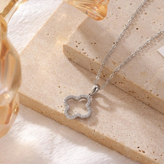 Silver necklace with a clover-shaped pendant on a beige surface