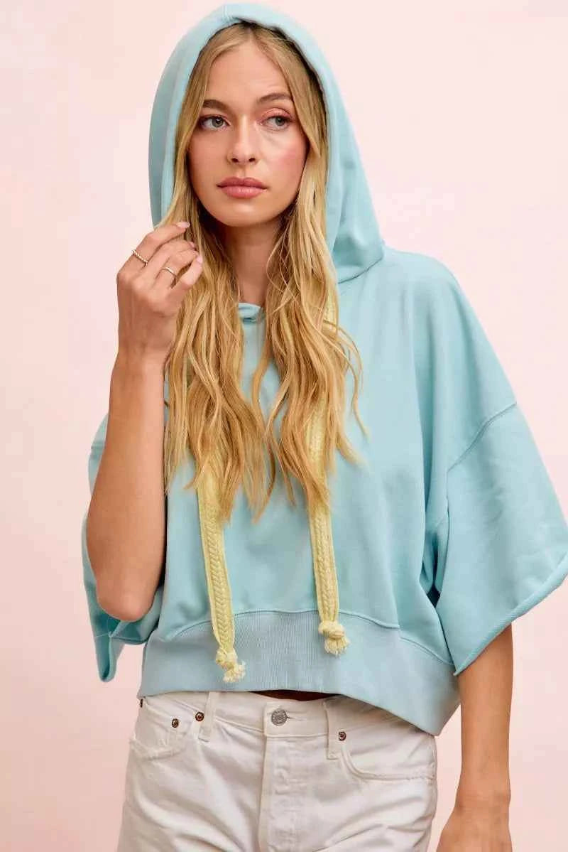Woman wearing a light blue washed terry short sleeve hoodie top with drawstring hood and relaxed oversized fit by BiBi.